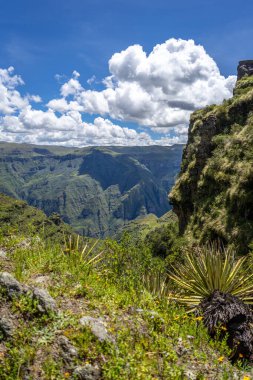 Waqrapukara arkeolojik alanını çevreleyen yeşil dağ tepeleri ve sarp kayalıklar, And 'ın berrak mavi gökyüzü altında nefes kesici panoramik manzaralar sunuyor.