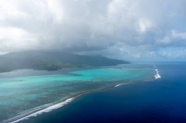 Fransız Polinezyası 'ndaki Raiatea adasının nefes kesici hava manzarası, berrak turkuaz sular, yemyeşil dağlar ve kıyı boyunca uzanan botlar sergileniyor.