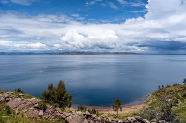 Tarım tarlaları, Taquile Adası 'ndaki yemyeşil sularla harmanlanmış. Titicaca Gölü' nün derin mavi sularına tepeden bakan engin bulutlu bir gökyüzünün altında.