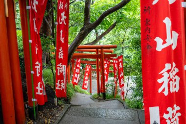 Japonya 'nın Kamakura kentindeki Tsurugaoka Hachiman-gu türbesi içine yerleştirilmiş Maruyama Inari Tapınağı' na giden yol parlak kırmızı torii kapıları ve sancaklarla çevrilidir.