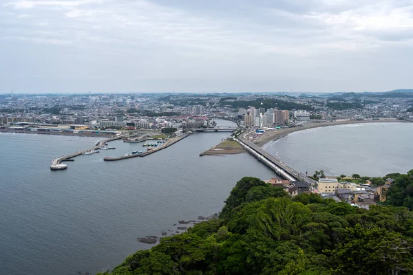 Adadan Enoshima şehrine bakan geniş bir kıyı manzarası kıvrımlı körfez, kentsel ufuk çizgisi, liman ve etrafındaki orman tepelerini ortaya çıkarıyor. Japonya