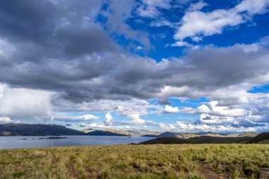 Peru 'daki Lagunillas Gölü, üzerinde kara fırtına bulutları ve dağların üzerine yağan yağmur yağmuru ile yuvarlanan tepeler ve otlaklarla çevrilidir.