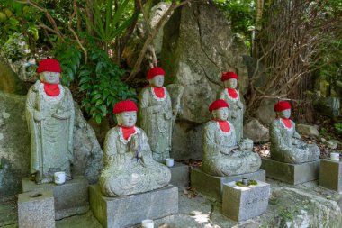 Japonya 'nın Hiroşima kentindeki Mitaki-Dera tapınağında huzurlu bir ormanda. Jizo Bosatsu heykelleri koruma ve hatırayı simgeleyen kırmızı örgülü şapkalar giyerler.