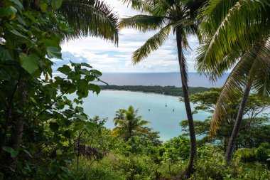 Fransız Polinezyası, Maupiti 'deki Teurafaatiu Dağı' ndan nefes kesici bir manzara, turkuaz gölüne tepeden bakan, yemyeşil tropikal bitki örtüsünün çerçevelediği bir motu yakınındaki yelkenli.