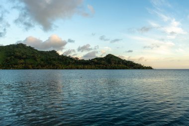 Günbatımının ılık parıltısı Hurepiti Körfezi 'nin sakin sularından yansıyor. Fransız Polinezyası' nın Tahaa Adası 'ndaki yemyeşil tepelerle çevrili.