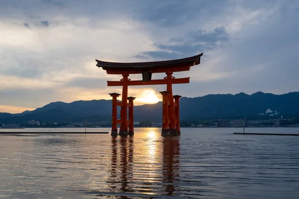 Itsukushima jinja Tapınağı 'nın ünlü yüzen torii kapısı Miyajima Adası yakınlarında sakin suları ve çevresini çevreleyen yeşil tepeleri olan günbatımında. Japonya, Hiroşima yakınlarında.