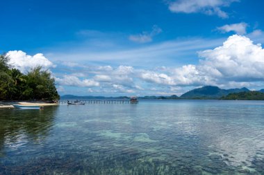 Bolilanga Adası, Togian takımadaları, Sulawesi, Endonezya 'nın sakin sularına doğru uzanan uzun ve ahşap bir iskele mavi gökyüzünün altında bir tekne.