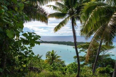 Fransız Polinezyası, Maupiti 'deki Teurafaatiu Dağı' ndan nefes kesici bir manzara, turkuaz gölüne tepeden bakan, yemyeşil tropikal bitki örtüsünün çerçevelediği bir motu yakınındaki yelkenli.