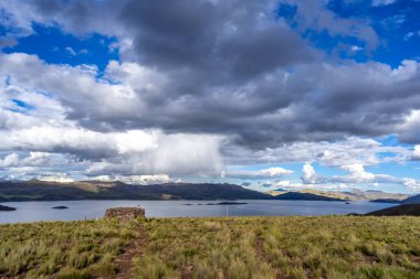Peru 'daki Lagunillas Gölü, üzerinde kara fırtına bulutları ve dağların üzerine yağan yağmur yağmuru ile yuvarlanan tepeler ve otlaklarla çevrilidir.