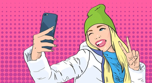 Mujer en sombrero Chaqueta de invierno Tomando foto selfie Teléfono inteligente Gesto de la paz Pop Art estilo retro — Vector de stock