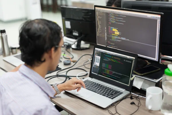 Desenvolvedor de software terceirizado asiático que olha a tela sentada na mesa — Fotografia de Stock