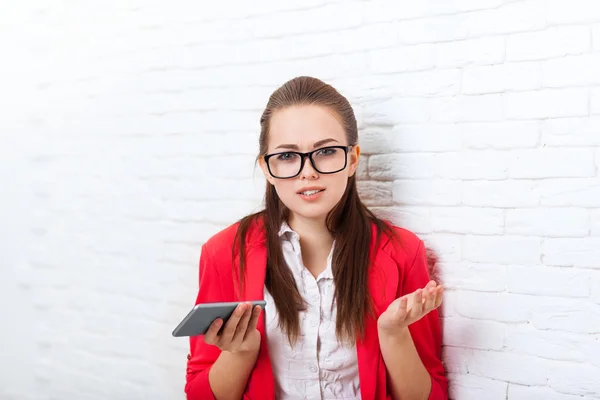Mujer de negocios inseguro, dudoso celebrar teléfono inteligente celular usar gafas chaqueta roja acentuado gesto problema —  Fotos de Stock