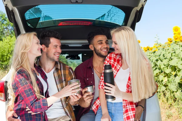 Amigos bebendo chá segurando copos de café thermos sentado no carro tronco ao ar livre campo — Fotografia de Stock