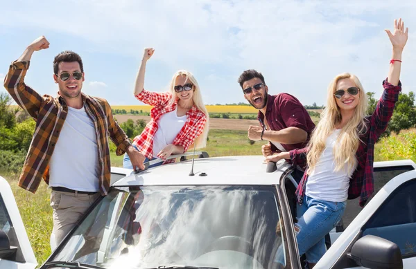 Amigos emocionados en el techo del coche campo al aire libre levantan los brazos la gente sonríe — Foto de Stock