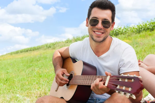 Jeune homme jouant de la guitare journée d'été assis herbe verte pique-nique extérieur — Photo