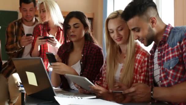 Tablet bilgisayar akıllı telefon kullanan öğrenciler oturma masası tartışırken gülümseme insanlar grup — Stok video