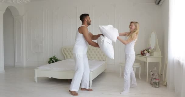 Couple fighting pillows bedroom mix race man woman playing having fun together — Stock Video