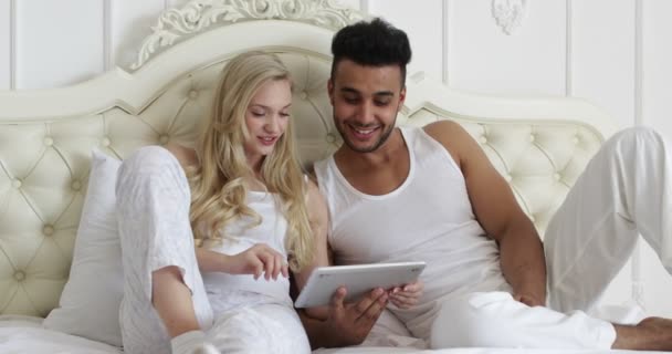 Couple couché lit en utilisant tablette, mélanger course homme femme sourire matin chambre — Video