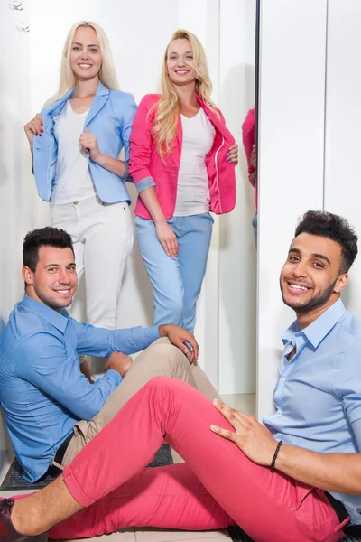 Молодые люди Модный магазин Примерочная магазин, счастливая улыбающаяся женщина пробуя новую одежду, мужчина сидит на полу — стоковое фото
