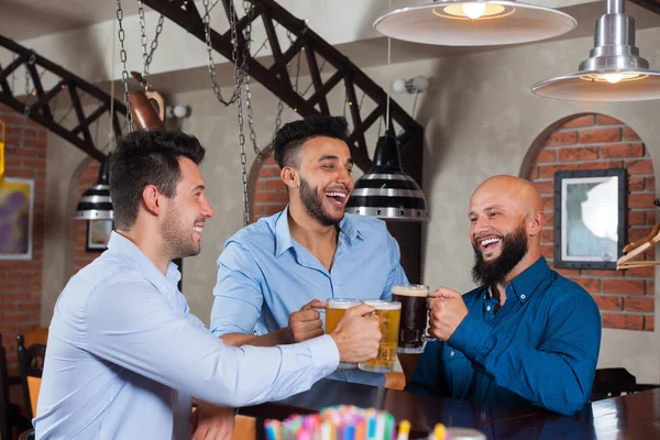Három ember in bar Clink szemüveg kenyérpirító, ivás Beer Hold bögrék, mix Race vidám barátok kopás ingek — Stock Fotó