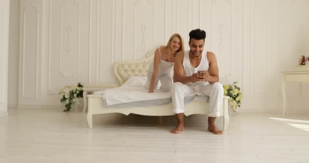 Coppia sdraiato letto utilizzando smart phone mix gara uomo donna divertirsi giocando abbraccio sorriso mattina camera da letto — Video Stock