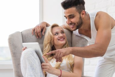 Young Woman Sit In Armchair Using Table Computer, Hispanic Man Point Finger To Screen