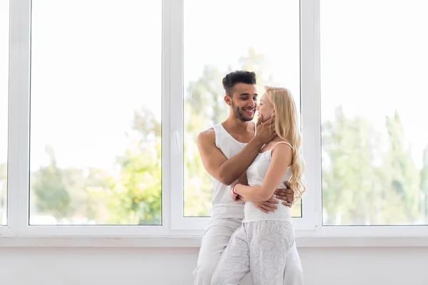 Junges schönes Paar steht am großen Fenster und umarmt sich küssend, glücklicher hispanischer Mann und Frau — Stockfoto