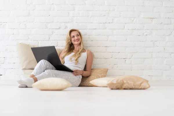 Mulher loira jovem sente-se no chão travesseiros usando computador portátil, linda menina feliz sorrindo olhar para cima para copiar espaço — Fotografia de Stock