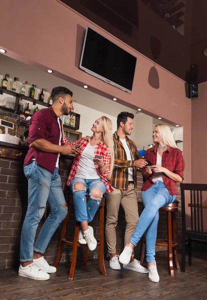 Mensen vrienden drinken sinaasappelsap praten lachen bij bar teller, mix ras man en vrouw paar volledige lengte — Stockfoto