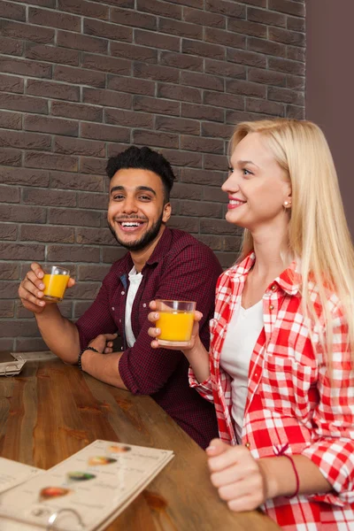Mix závodní muž a žena podržet brýle s pomerančovou šťávou u dřevěného stolu v baru Cafe — Stock fotografie