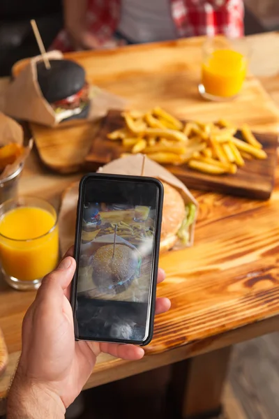 Homme à la main prenant des photos de hamburger de boeuf frit de pommes de terre Fast Food servi dans le café de table en bois de papier — Photo