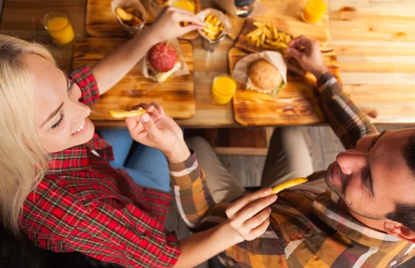 Молодий чоловік і жінка їдять картоплю швидкого харчування сидячи на дерев'яному столі в кафе Вид зверху кута — стокове фото