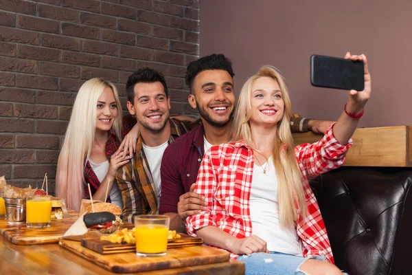 Gruppo di persone mangiare fast food hamburger patate seduti al tavolo di legno nel caffè scattare foto selfie — Foto Stock