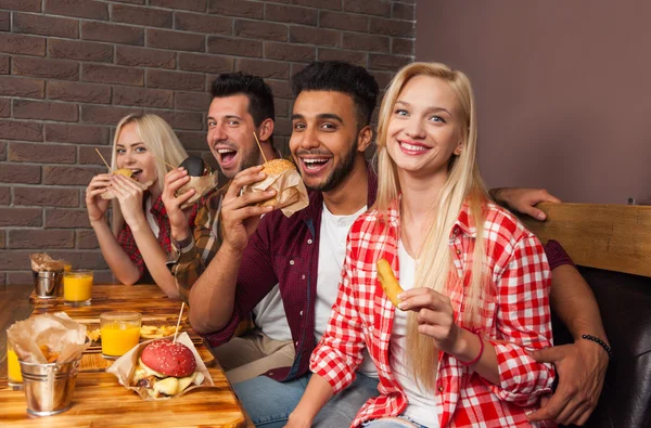 Lidé skupiny jíst Fast Food hamburgery u dřevěného stolu v Cafe — Stock fotografie