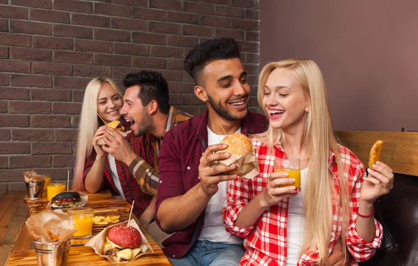 Mensen groep eten fastfood hamburgers aan houten tafel In Cafe — Stockfoto