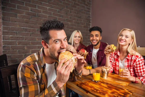 Mensen groep eten fastfood hamburgers aan houten tafel In Cafe — Stockfoto