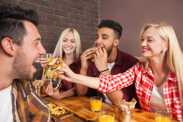 Mensen groep eten fastfood hamburgers aan houten tafel In Cafe — Stockfoto