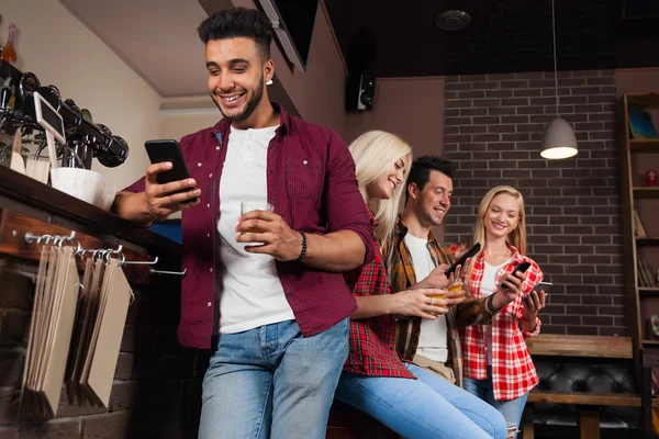 Amigos de la gente usando el teléfono inteligente celular, bebiendo jugo de naranja hablando riéndose sentado en el mostrador del bar, hombre y mujer de raza mixta —  Fotos de Stock