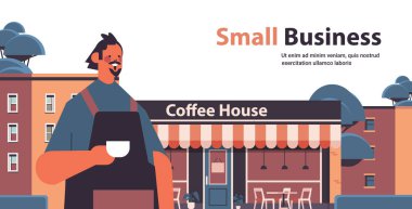 Üniformalı kahveci, önlüklü, kahve dükkanının yatay portresinin yanında duran erkek barista.