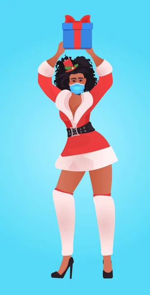 Africano americano santa mulher na máscara segurando caixa de presente ano novo Natal feriados celebração coronavírus quarentena conceito comprimento total vertical vetor ilustração — Vetor de Stock