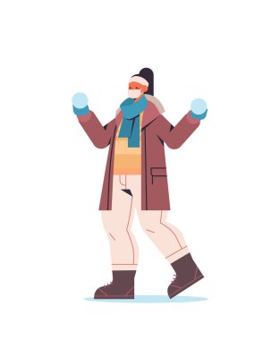 Kar topu tutan maskeli bir kız kış eğlencesine çıkan bir kadın. Coronavirüs karantina konsepti.