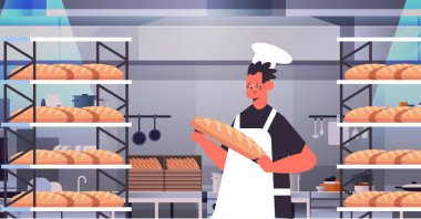 Üniformalı erkek fırıncı elinde ekmek fırını ürünleriyle üretim konsepti portresi yapıyor.