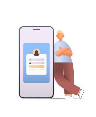 Akıllı telefon kullanan genç adam büyük cep telefonunun yanında dikey olarak dikey duruyor.