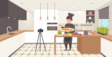 Üniformalı bir yemek blogcusu mutfakta pizza pişiriyor. Şef, tripod blogunda kamera ile video blogu kaydediyor.