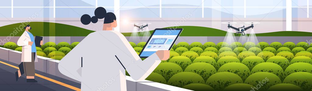 engineers controlling agricultural drones sprayers quad copters flying to spray chemical fertilizers in greenhouse