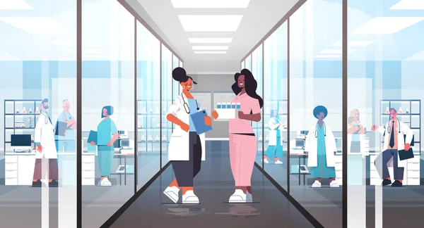 Mieszaj lekarzy wyścigowych w mundurach dyskutujących podczas spotkania w szpitalnym korytarzu koncepcja opieki zdrowotnej — Wektor stockowy