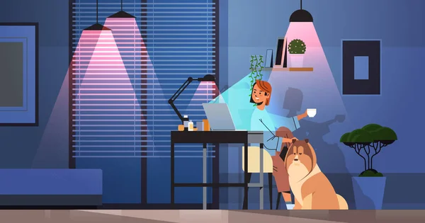 Mujer de negocios freelancer mirando a la mujer de la pantalla del ordenador portátil sentado en el lugar de trabajo cerca de perro en habitación oscura noche — Archivo Imágenes Vectoriales