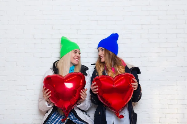 Duas meninas amigos olham um para o outro com balões de forma de coração vermelho Dia dos Namorados — Fotografia de Stock