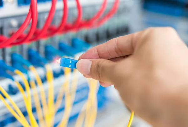 man working in network server room with fiber optic hub for digital communications and internet