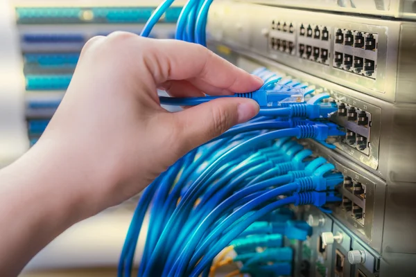 Hand met netwerkkabels aangesloten op servers in een datacenter — Stockfoto